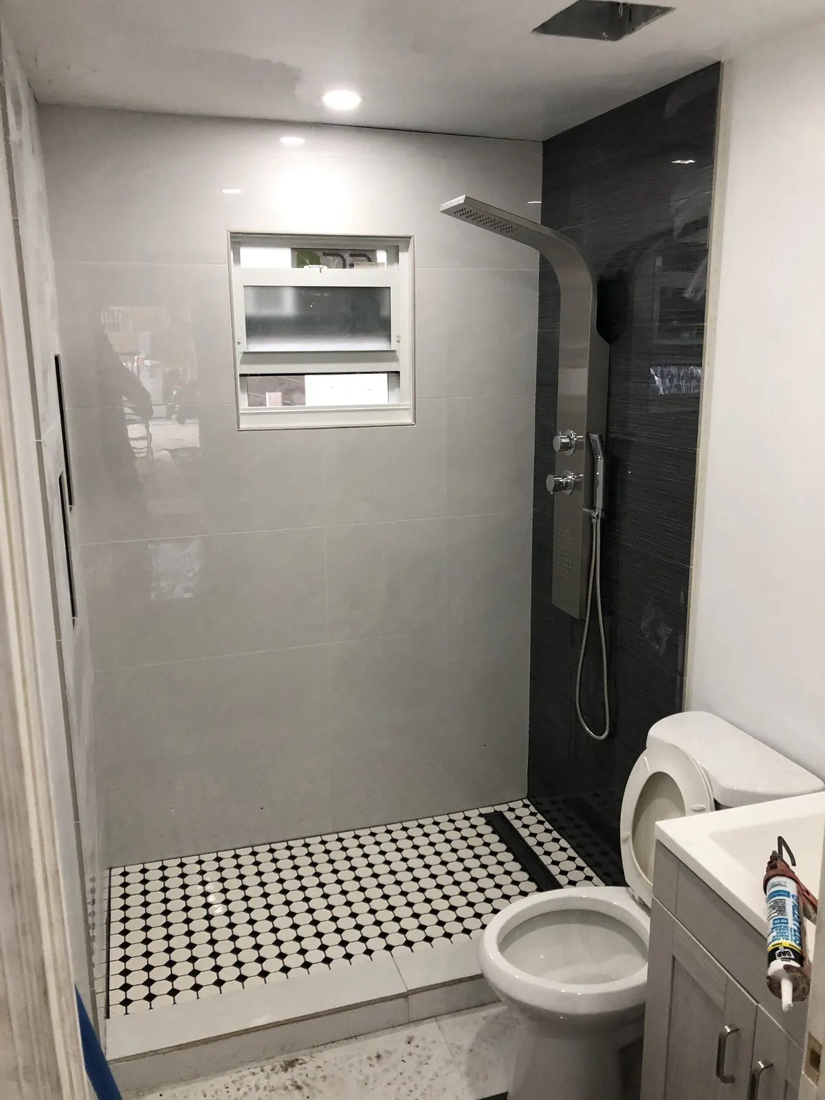 Shower with black-and-white mosaic floor, toilet, and small window.