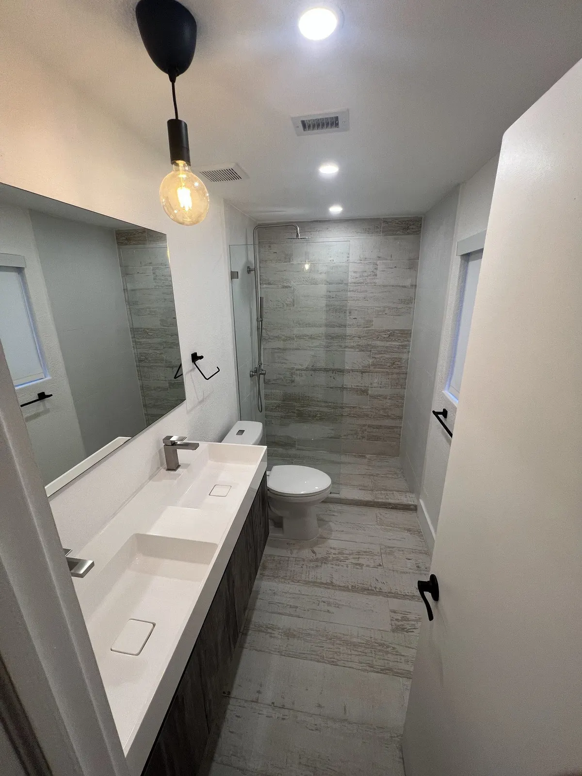 Long narrow bathroom corridor with dual sink vanity and pendant lighting.