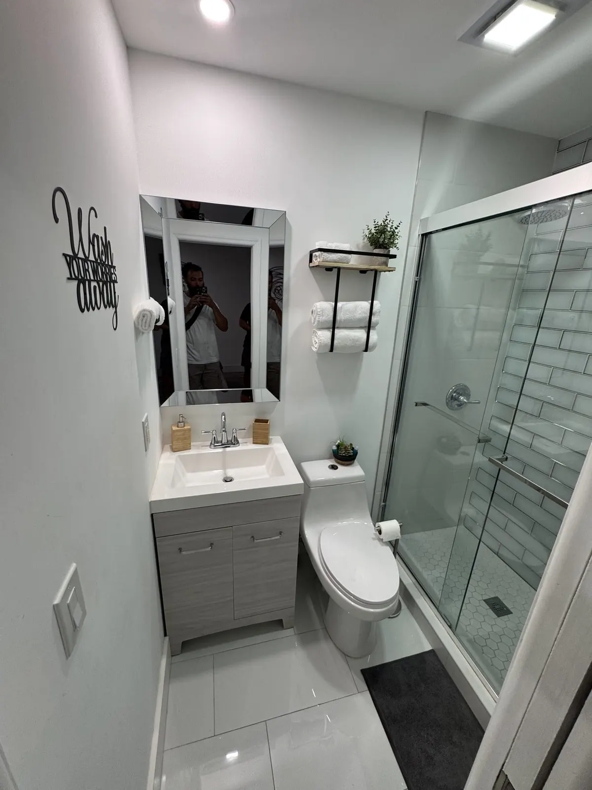 Compact white bathroom with glass shower enclosure and narrow vanity.
