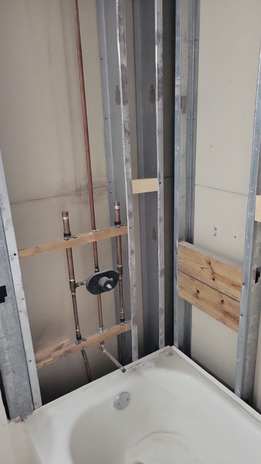 Bathtub area during renovation with exposed studs and visible plumbing.