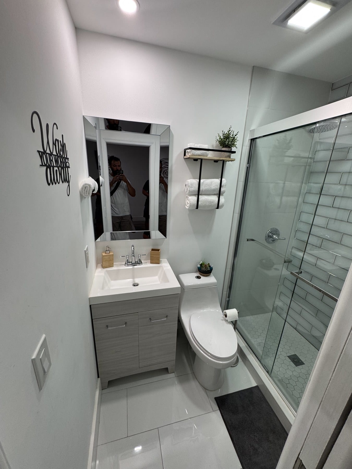 Compact white bathroom with glass shower enclosure and narrow vanity.