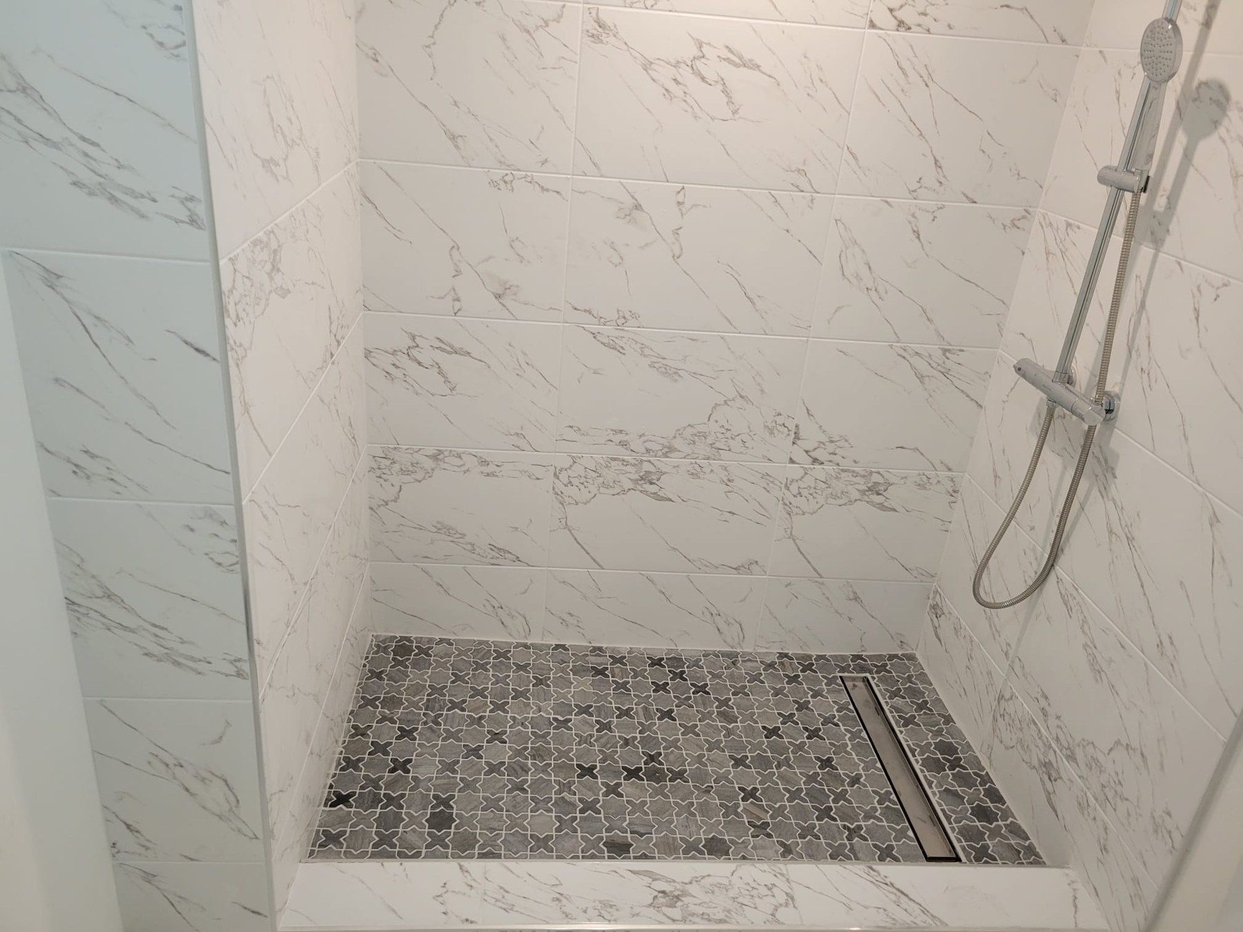 Shower with white marble-look wall tile and black-and-white mosaic floor.