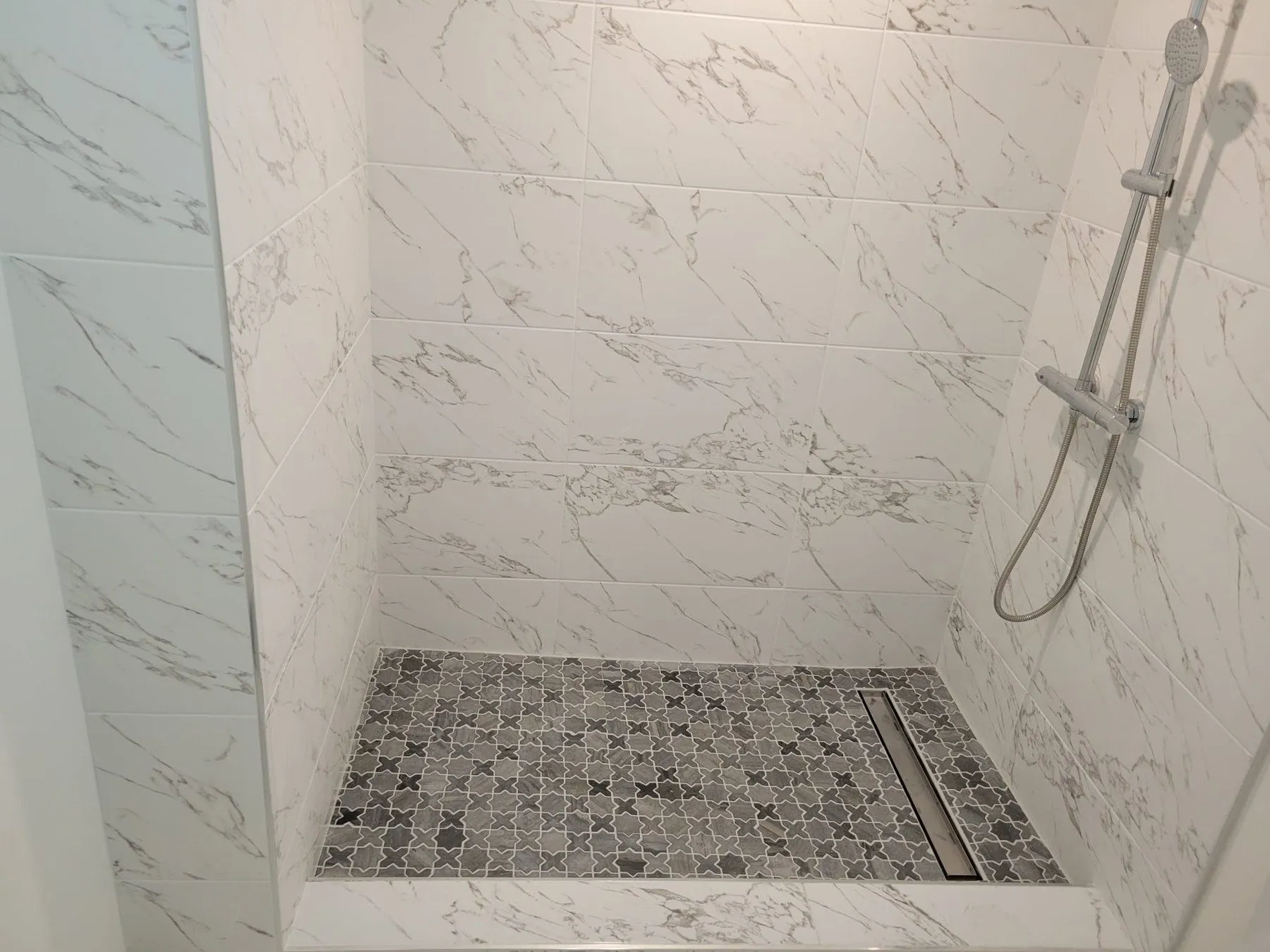 Shower with white marble-look wall tile and black-and-white mosaic floor.