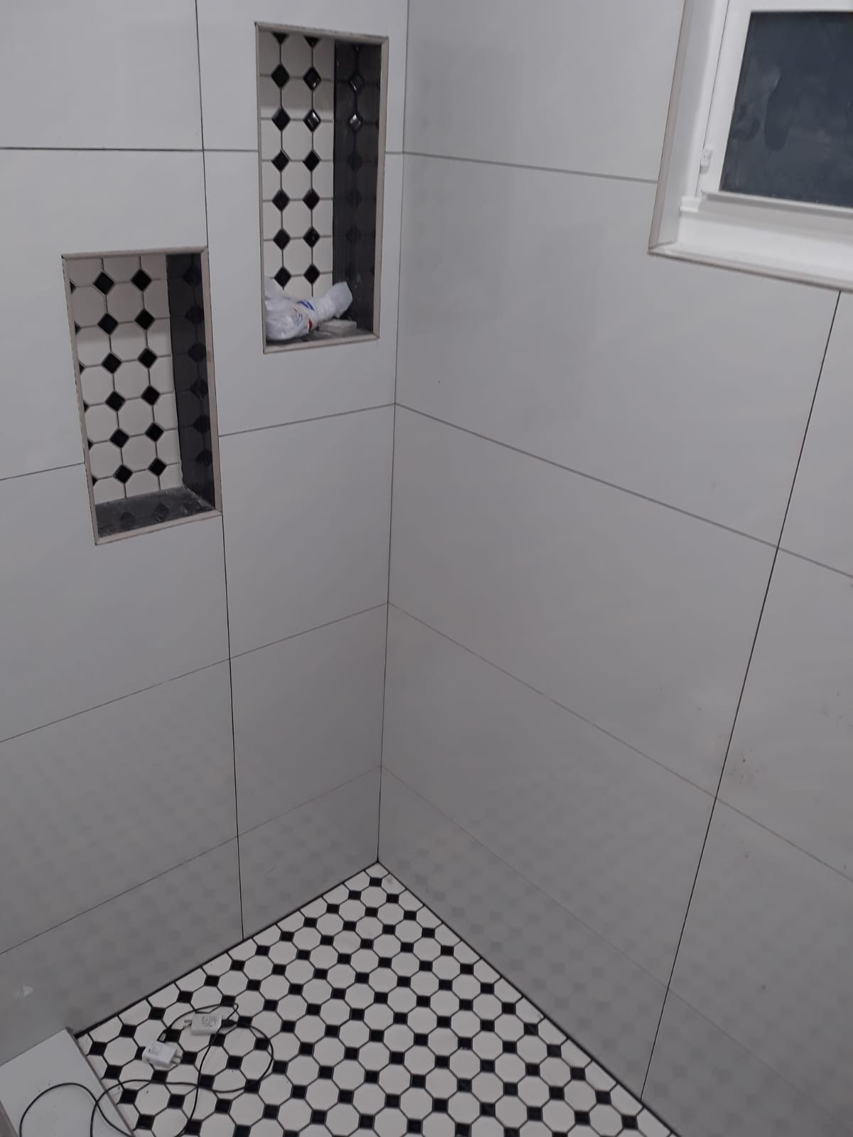 Shower corner with large white tiles, recessed niche, and hex mosaic floor.