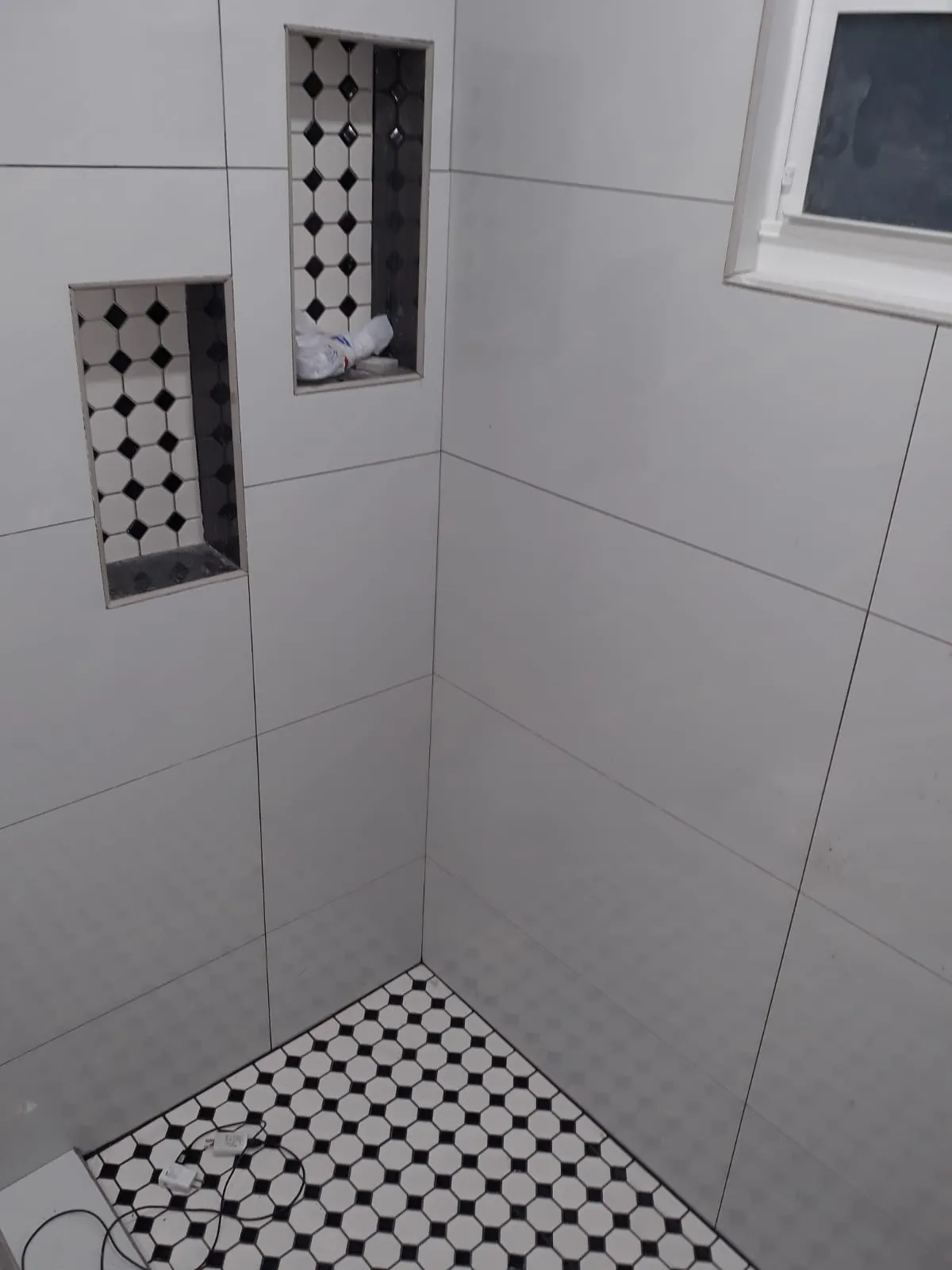 Shower corner with large white tiles, recessed niche, and hex mosaic floor.