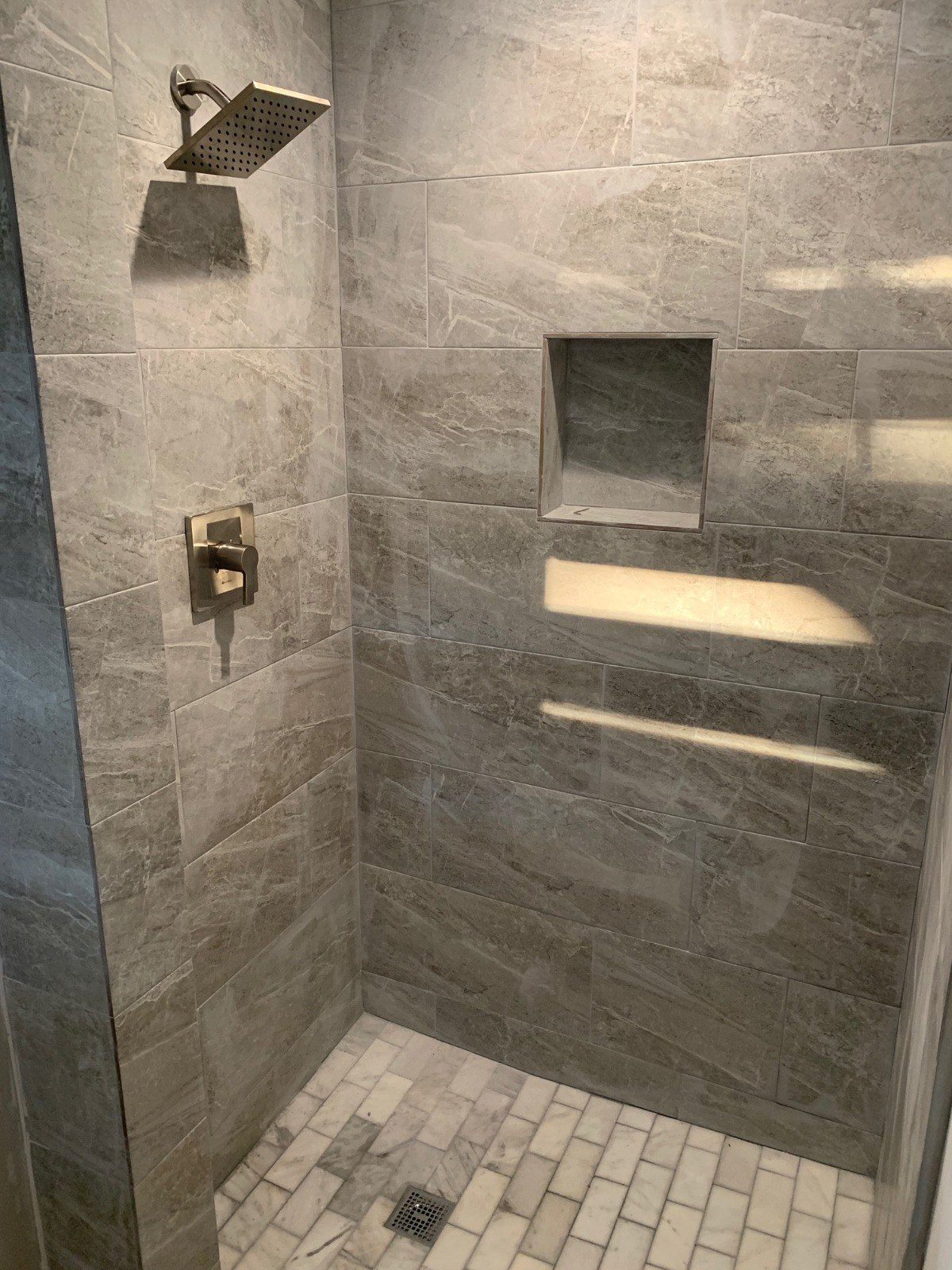 Gray tiled shower with built-in niches and overhead rain shower head.