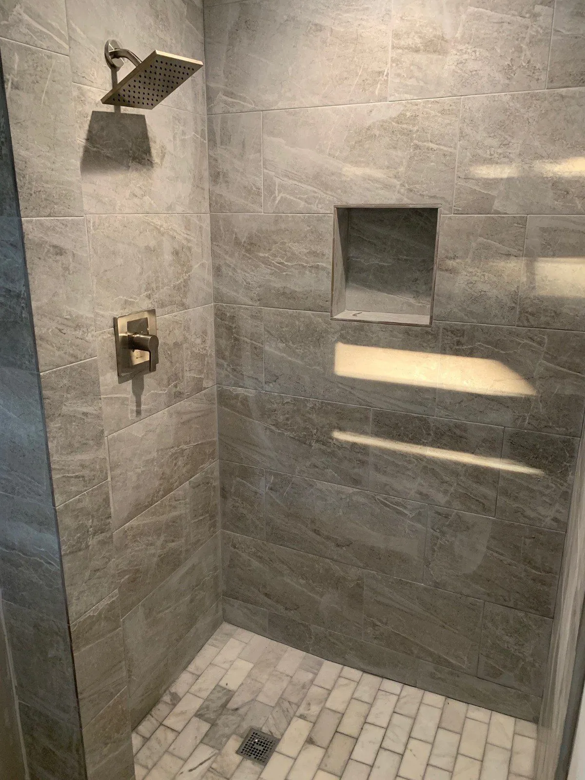 Gray tiled shower with built-in niches and overhead rain shower head.