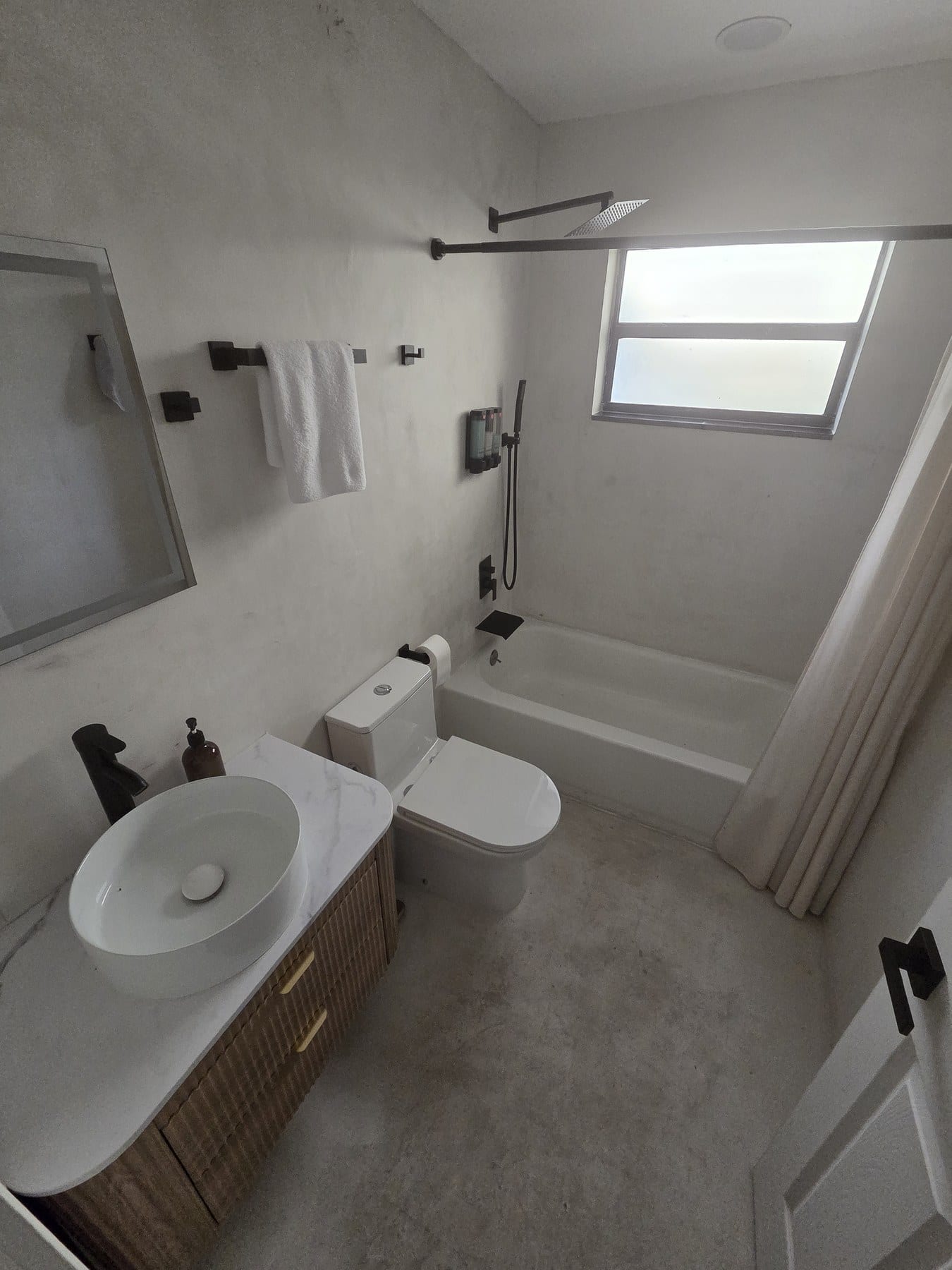 Compact bathroom with round vessel sink, toilet, and light gray tile walls.
