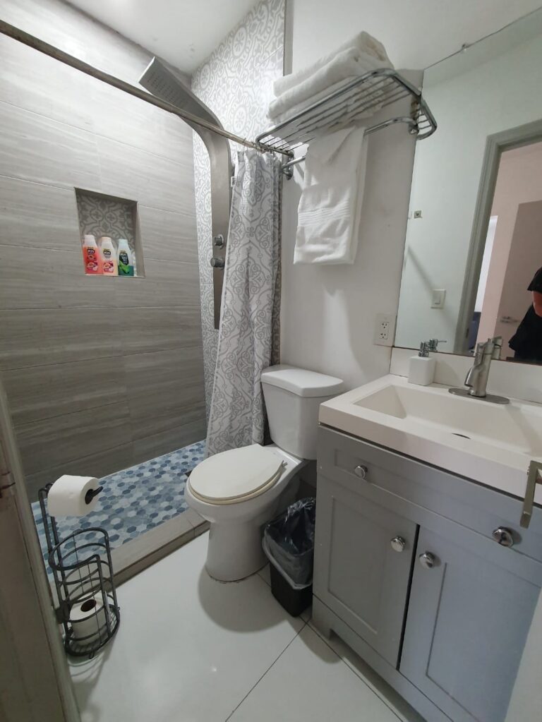 Narrow bathroom with shower curtain, toilet, and white vanity.