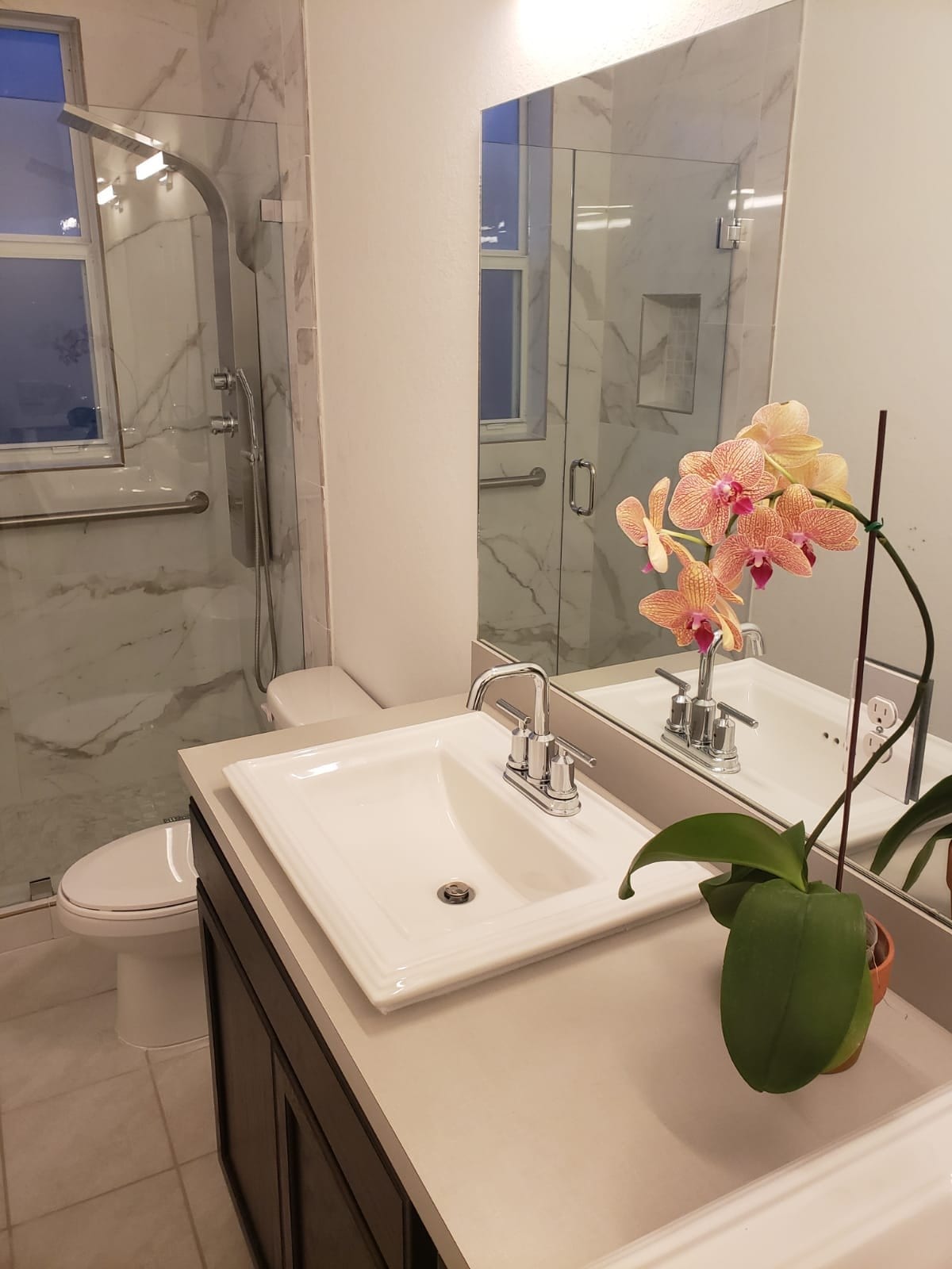 Single-sink vanity with white countertop, mirror, and potted orchid.