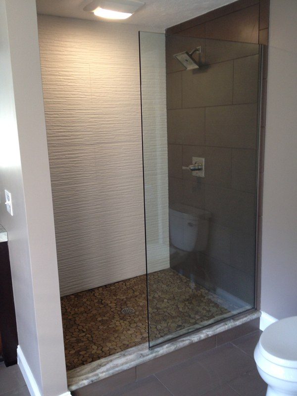 Frameless glass shower with pebble-style floor and adjacent toilet.