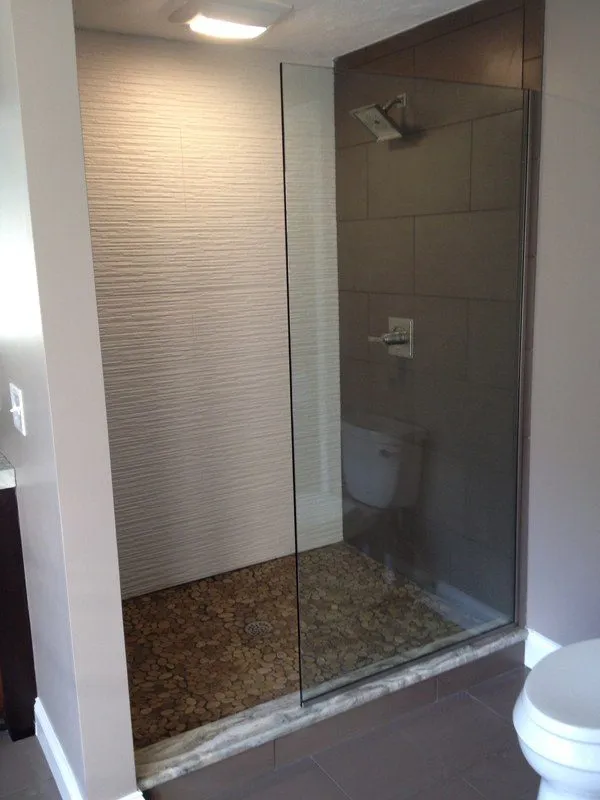 Frameless glass shower with pebble-style floor and adjacent toilet.