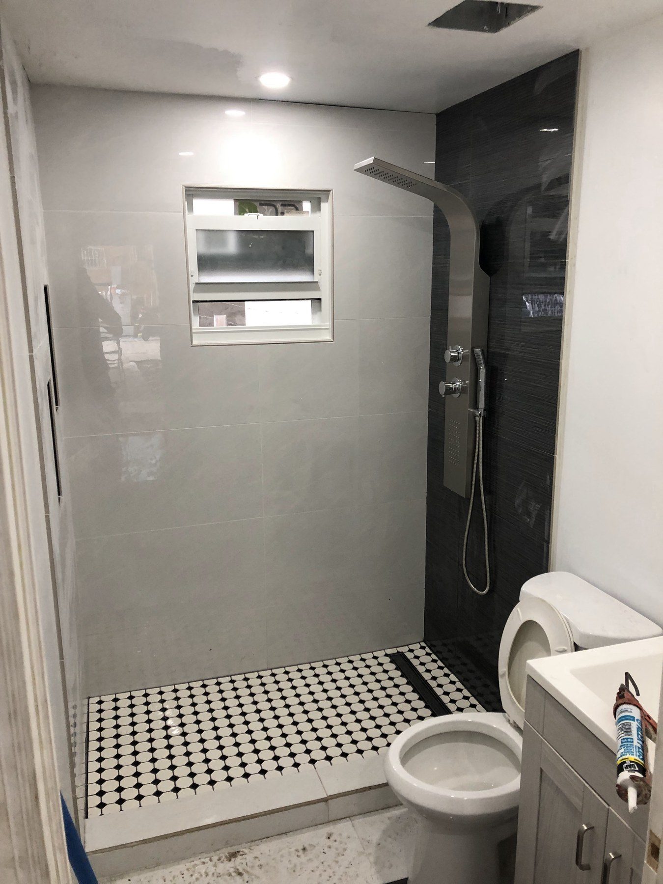 Shower with black-and-white mosaic floor, toilet, and small window.