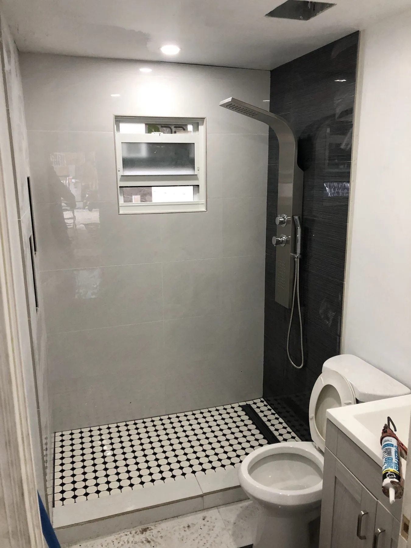 Shower with black-and-white mosaic floor, toilet, and small window.