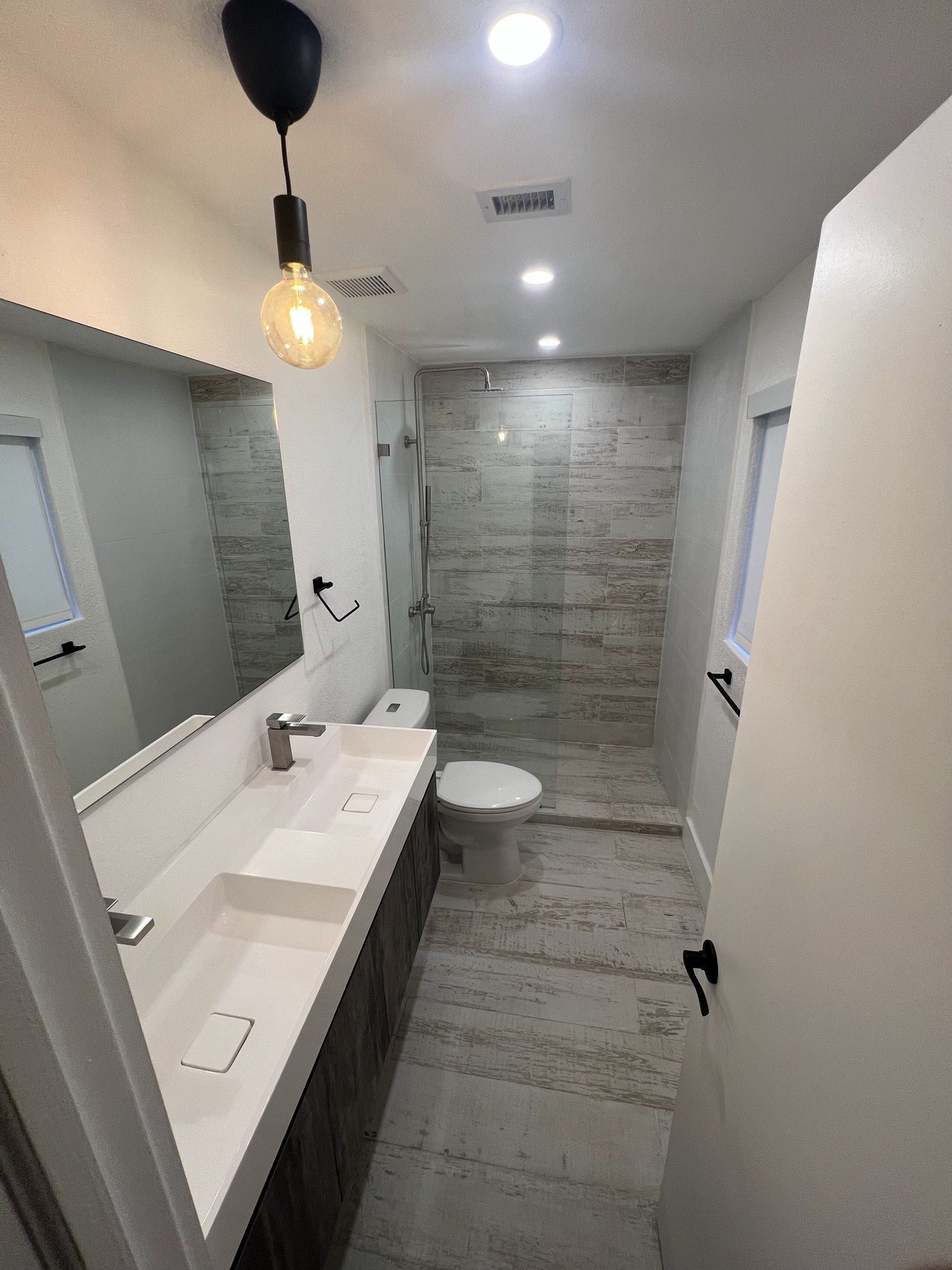 Long narrow bathroom corridor with dual sink vanity and pendant lighting.