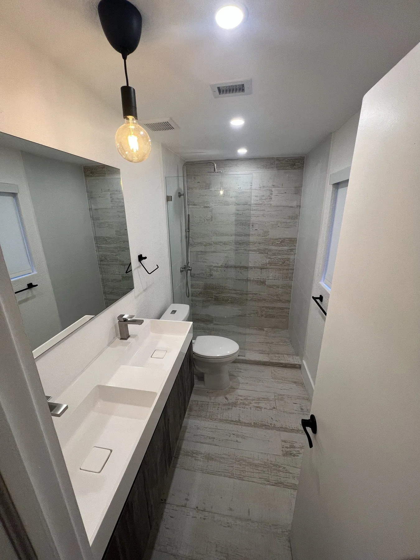 Long narrow bathroom corridor with dual sink vanity and pendant lighting.